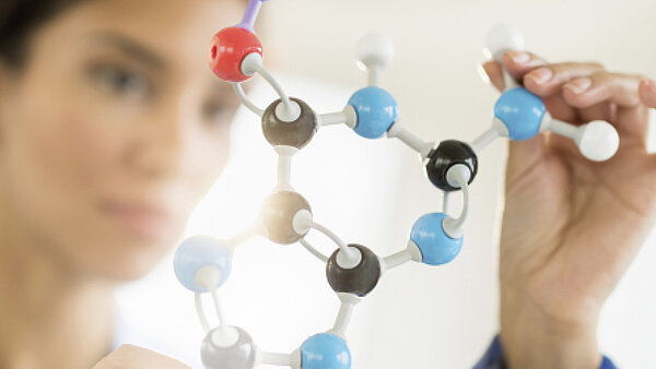 Frau in der klinischen Forschung schaut prüfend auf ein Molekülmodell.